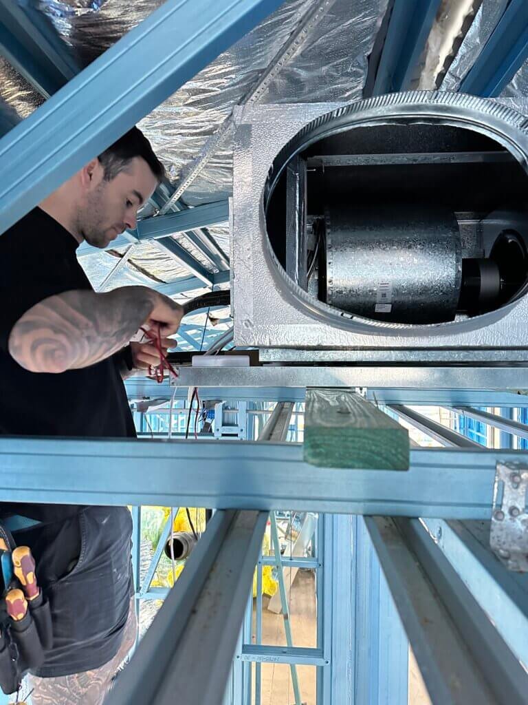 ⁠Technician performing electrical rough-in wiring on a ducted air conditioning indoor fan coil unit inside a steel frame house
